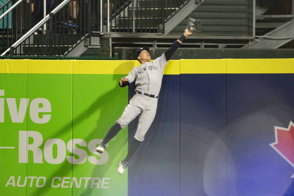 Aaron Judge reaches his left arm and glove well over the outfield fence to take away a home run from Cavan Biggio of the Blue Jays in 2021