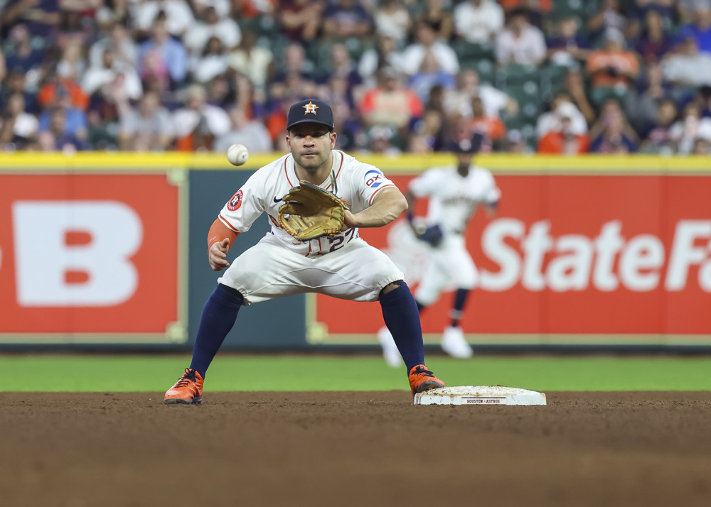 Jose Altuve, in white jersey and pants, prepares to catch a throw from his third baseman