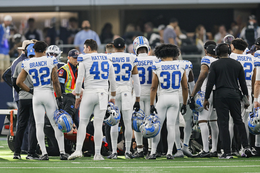 Detroit Lions players surround Aidan Hutchinson as Hutchinson is placed on a cart following his season-ending injury.