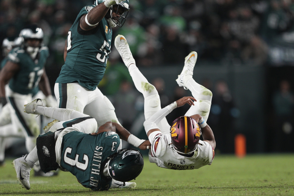 Jayden Daniels is about to fall on his back after being tackled by an Eagles player.