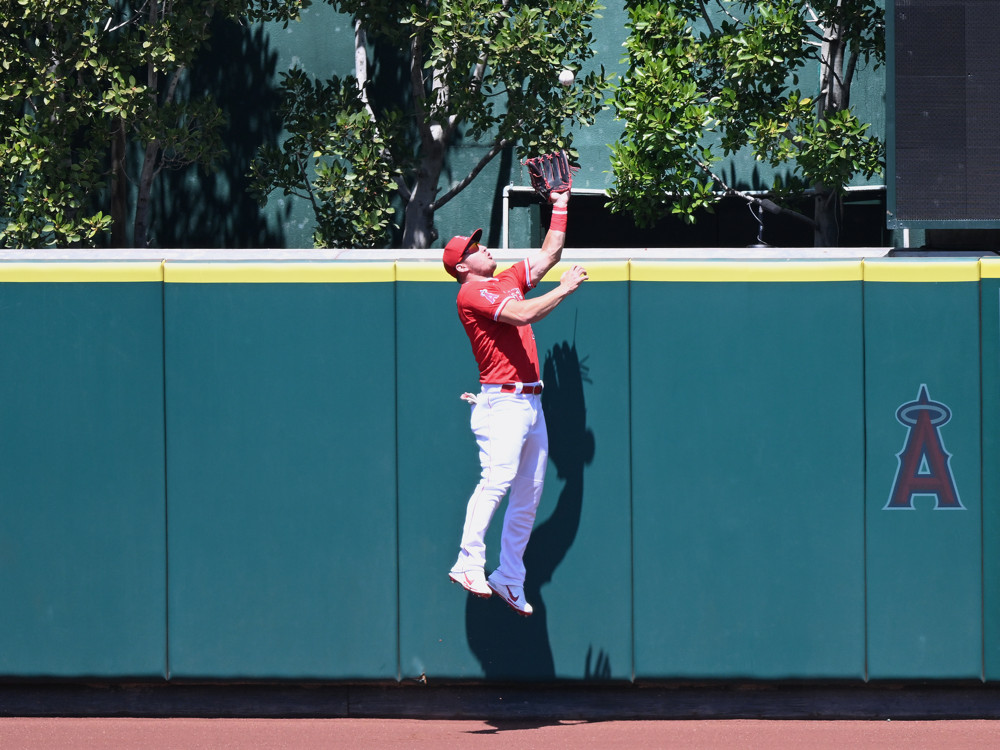 Mike Trout jumps at the outfield fence as a ball descends near his glove.