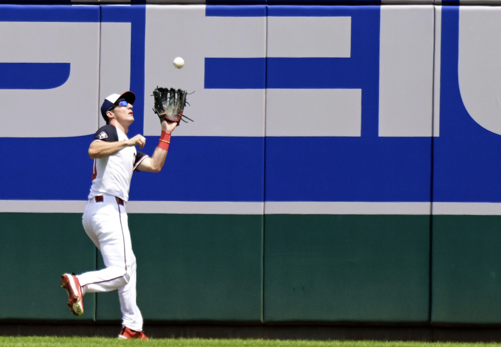 Jacob Young is back near the outfield fence and has his glove up as he prepares to catch a fly ball that has almost completed its descent.