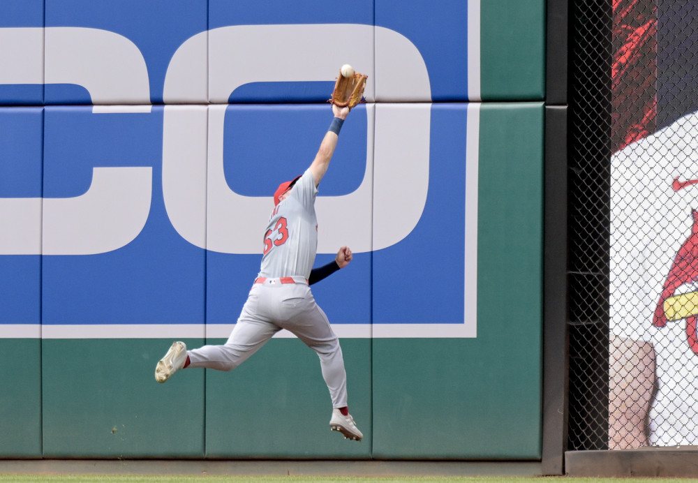 Michael Siani reaches up with his gloved hand (right hand) to make a reaching catch. Both feet are off the ground, the right foot closer to the wall, the left foot kicking back.