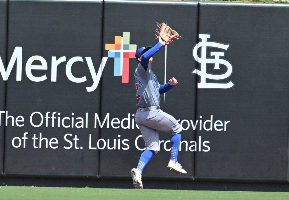 Pete Crow-Armstrong retreats as he prepares to catch a fly ball near the outfield fence in Busch Stadium. His right leg is raised and his left heel is up, with his toes down.