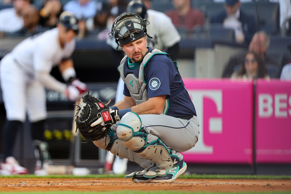 Cal Raleigh, in a catcher's crouch, looks to the dugout.