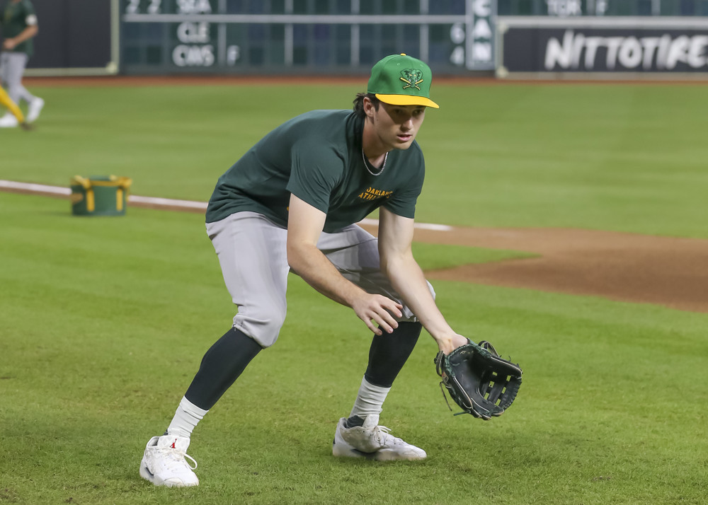 Jacob Wilson leans over in a ready position to field a ground ball prior to a game, while standing in foul territory near the dugout.