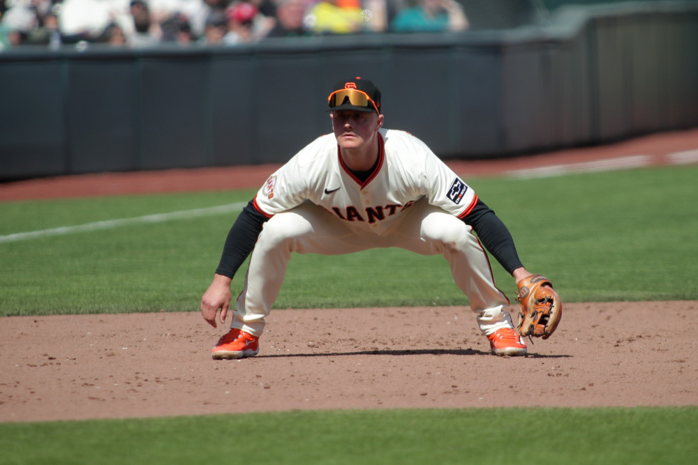 Matt Chapman, in white jersey and pants, squats into a ready position near third base.