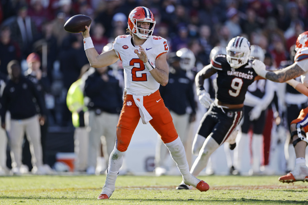 Cade Klubnik, wearing orange pants, white socks, a white shirt with an orange #2 and an orange helmet, brings his arm back to throw a pass.