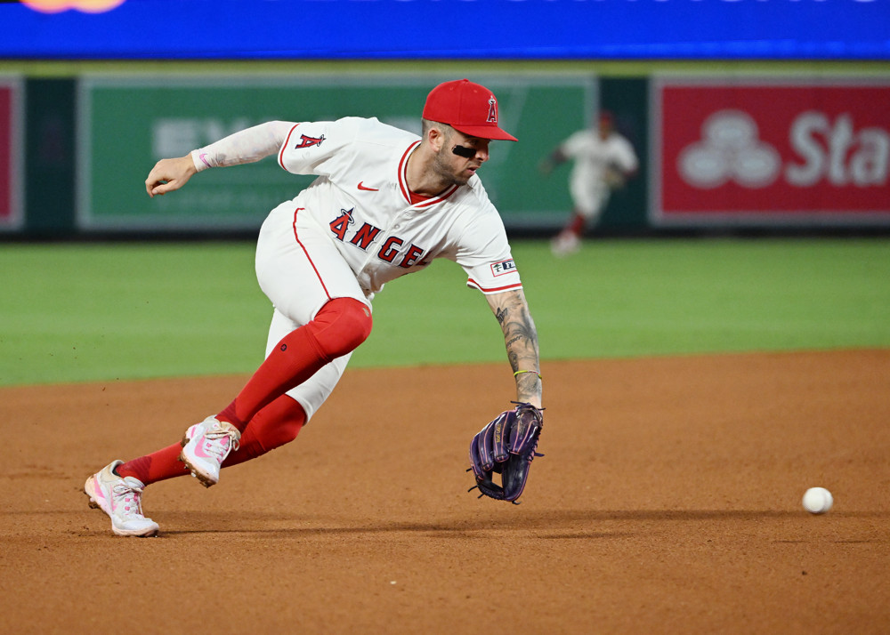 Zach Neto, in white Angels uniform and red cap and socks, backhands a ground ball at shortstop.