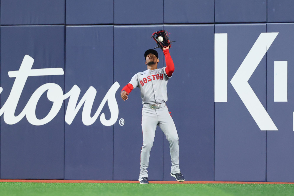 Ceddanne Rafaela, wearing a grey Red Sox jersey with Red Sox sewn across the front, reaches up with the glove on his left hand to make a catch.