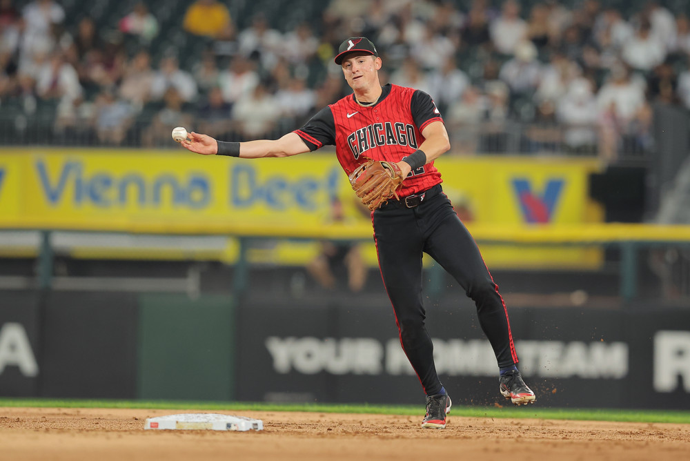 Colson Montgomery, wearing the White Sox alternate red jerseys (almost a tank top) with Chicago written across the front, black pants and a black cap, makes a sidearm throw from the shortstop position.