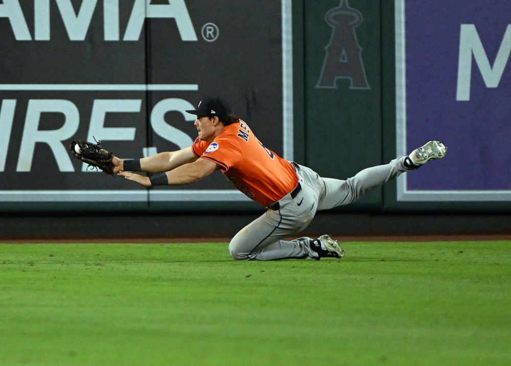 Jake Meyers, wearing an orange baseball jersey and grey pants, dives to his left and stretches out to make a catch.