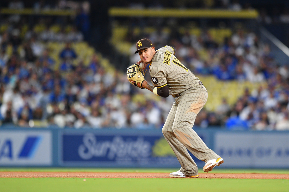 Manny Machado, in a grey Padres uniform and brown hat, prepares to make a throw to first base.