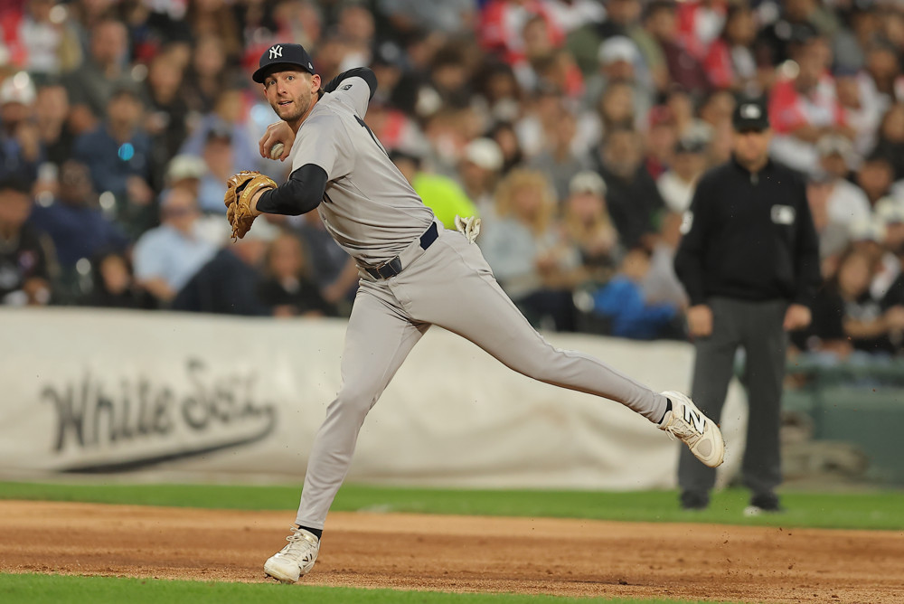 Third baseman Ryan McMahon, wearing a grey Yankees jersey and black Yankees cap, winds up to make a throw to first base. His right foot is down and his left foot is raised and he's trying to stay balanced as he throws.