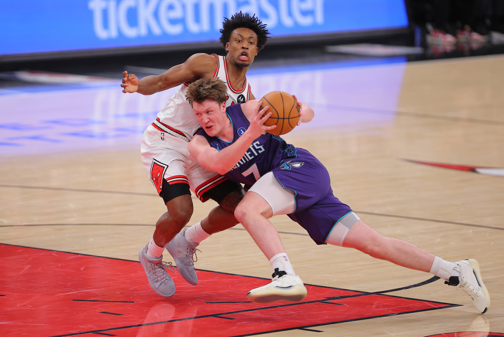 Kon Kneuppel, in blue jersey and shorts, leans into a Bulls defender as he holds the ball out behind him and tries to drive to the basket.