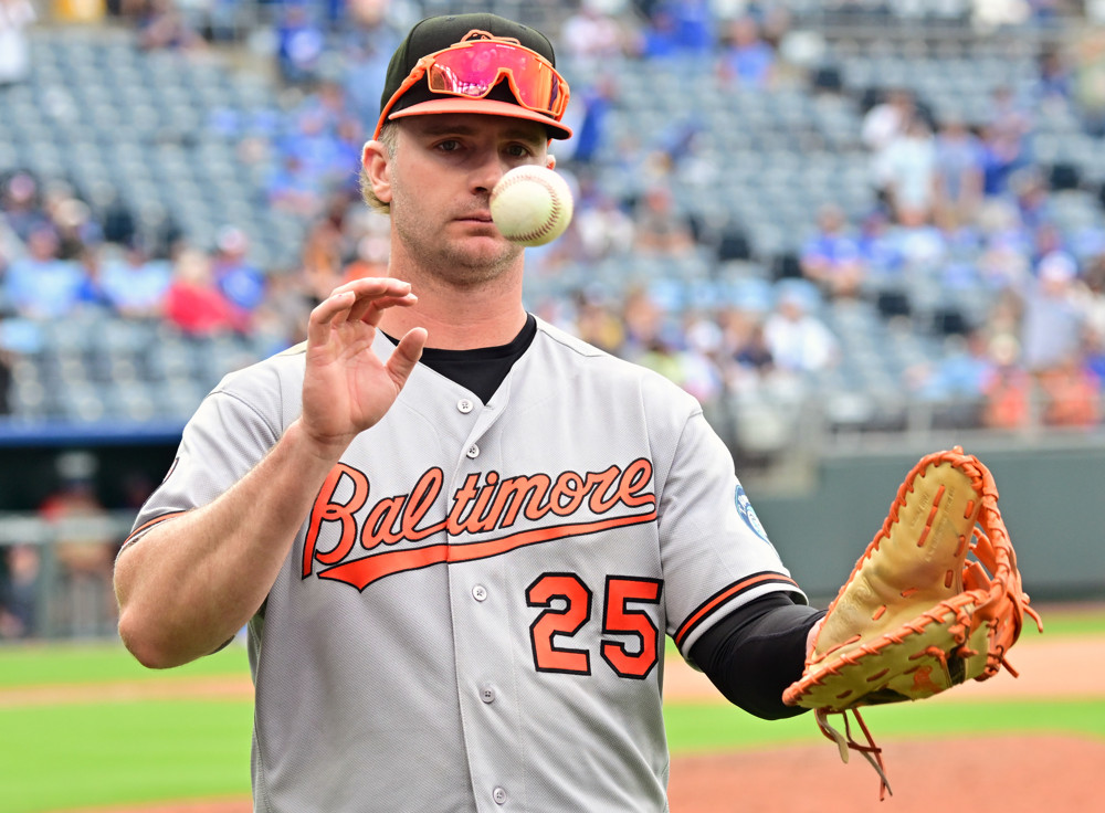 Pete Alonso flips a ball from his right hand to his glove as he walks back to the dugout. He's wearing a grey Orioles jersey with Baltimore 26 in script.