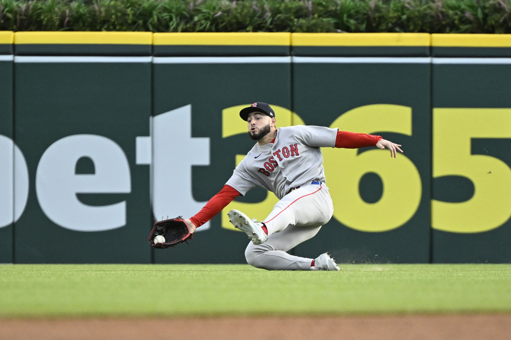 Wilyer Abreu of the Red Sox, in grey road jersey and pants and a red undershirt, makes a sliding catch, with his glove holding the ball just a few inches from the grass.