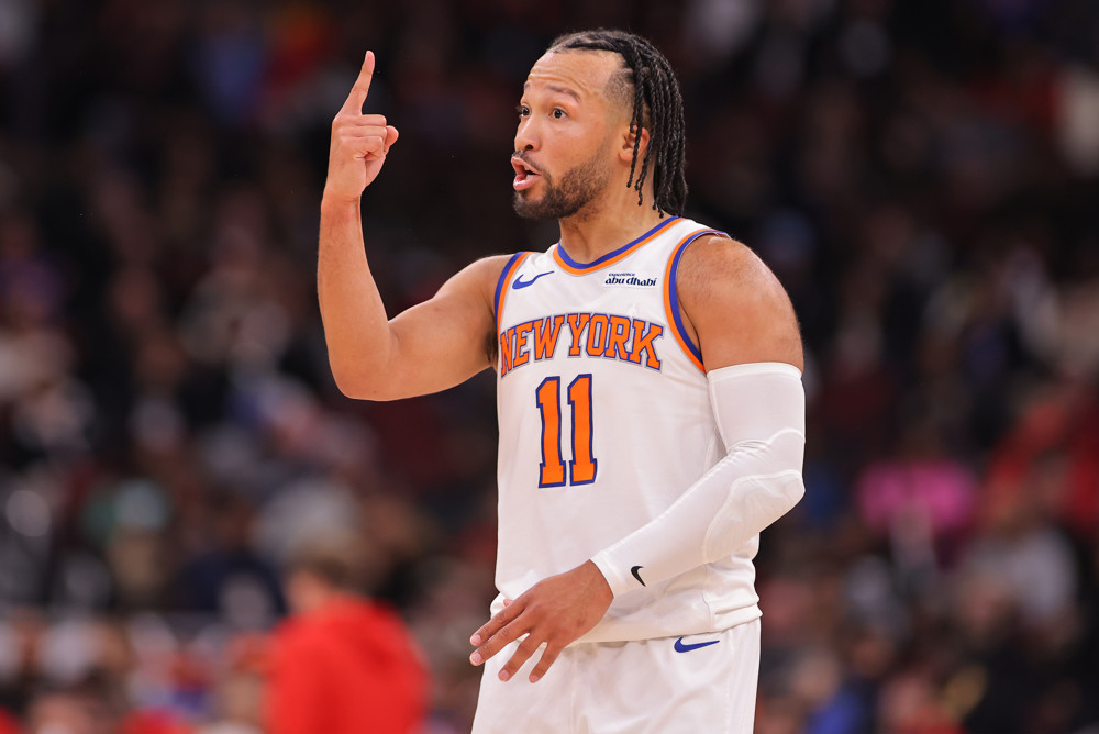 Jalen Brunson, wearing a white #11 New York Knicks jersey, raises his right index finger.
